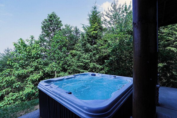 A hot tub surrounded by lush greenery. - Spacious Log Home w/ Game Room & Hot Tub (Sevierville)