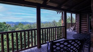 A wooden deck with a view of mountains, a covered seating area, and a log cabin structure. - Spacious Log Home w/ Game Room & Hot Tub (Sevierville)