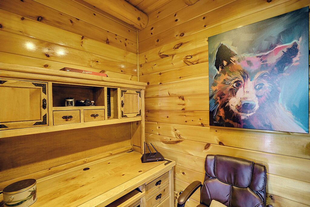 A wooden cabin interior with a desk, drawers, a chair, and a painting of a dog.
