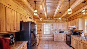 A log cabin kitchen with wooden cabinets, a refrigerator, a stove, and granite countertops. - Spacious Log Home w/ Game Room & Hot Tub (Sevierville)