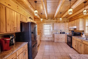Cocina de cabaña de troncos con armarios de madera, un refrigerador, una estufa y encimeras de granito.