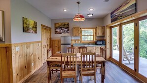 A wooden-paneled kitchen with a dining table and chairs, a refrigerator, and a window overlooking greenery. - Spacious Log Home w/ Game Room & Hot Tub (Sevierville)