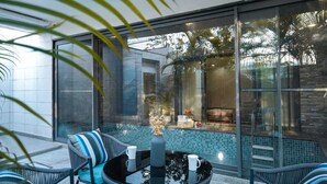 Un espace extérieur moderne, aménagé avec des meubles en osier, une piscine protégée par des parois de verre, et offrant une vue sur la piscine et l’immeuble voisin.