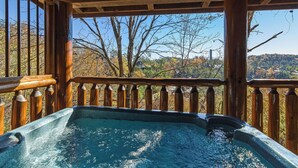 Un jacuzzi con cubierta de madera y barandilla, con vista a un paisaje pintoresco con árboles y colinas.