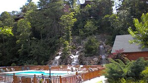 Un patio trasero con piscina, terraza de madera y una cascada.
