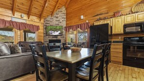 Interior acogedor de una cabaña con chimenea de piedra, techo de madera y comedor con mesa y sillas.