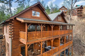 A log cabin with a balcony, a hot tub, and a stone wall.