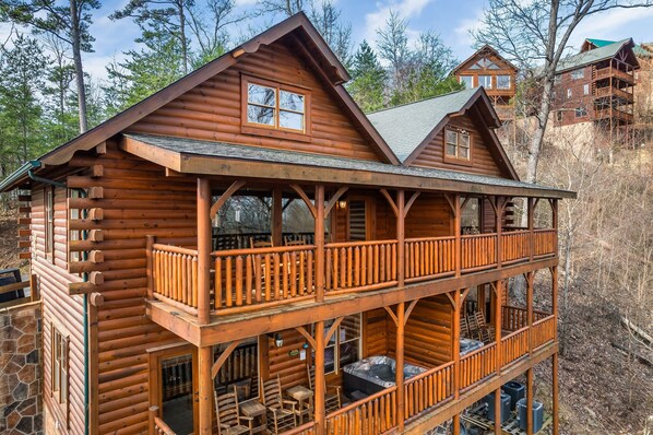 A log cabin with a balcony, a hot tub, and a stone wall.