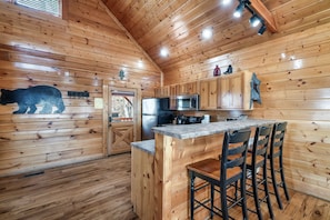A wooden cabin interior with a kitchen, a bear silhouette on the wall, and a bar area.