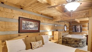 Un dormitorio de cabaña de madera con una cama, una mesita de noche, un aparador, un cuadro enmarcado, un reloj y una bañera de hidromasaje de piedra.