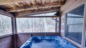 Una cabaña de madera con jacuzzi, ventanas amplias y vistas a un bosque.