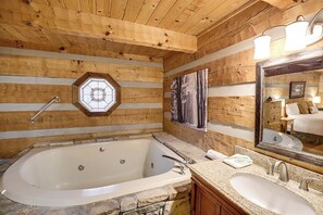 Een houten badkamer in een blokhutstijl, met een stenen wasbak, een ruim bad en houten wanden, en een zeshoekig raam.
