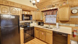 Una cocina con armarios de madera, un refrigerador negro, una estufa, un microondas y un lavavajillas.