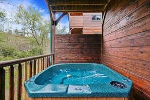 A wooden deck with a hot tub, wooden walls, and a view of a building in the background.