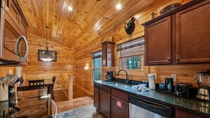 A wooden cabin interior with a kitchen area featuring a stove, sink, and cabinets.