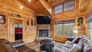A log cabin interior with a stone fireplace, leather couches, and a television.