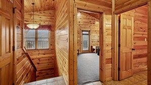 Ein Holzblockhaus-Interieur mit einer Treppe zu einem Schlafzimmer im zweiten Stock, einem kleinen Fenster mit Jalousien und einer Tür zu einem weiteren Raum.