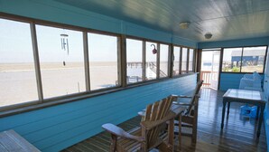 Una terrazza coperta con mobili in legno, ampie finestre vista spiaggia e vista sull'oceano.