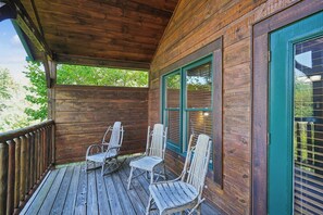 A wooden porch with two rocking chairs and a table. - Romantic Cabin w/ Hot Tub, Games & Fireplace (Gatlinburg)