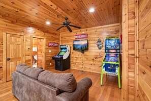 A cozy room with a sofa, a popcorn machine, a television, and arcade games. - Romantic Cabin w/ Hot Tub, Games & Fireplace (Gatlinburg)