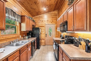 A wooden cabin interior with a kitchen featuring a refrigerator, stove, microwave, and sink. - Romantic Cabin w/ Hot Tub, Games & Fireplace (Gatlinburg)