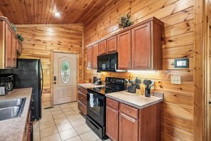 A kitchen with wooden walls, a black microwave, and a stainless steel sink. - Romantic Cabin w/ Hot Tub, Games & Fireplace (Gatlinburg)