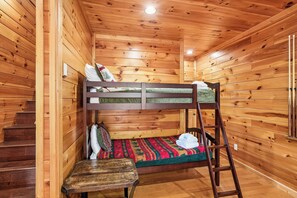 Una cama litera con escalera, una mesita pequeña y un tapete estampado en una habitación de madera con una escalera de madera.