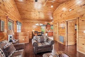 A log cabin interior with a dining area, a sofa, and a kitchen. - Romantic Cabin w/ Hot Tub, Games & Fireplace (Gatlinburg)