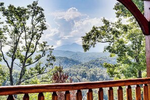 A wooden balcony with a view of a forested mountain range.
