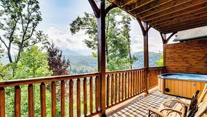 Eine Holzterrasse mit Whirlpool und Stühlen, mit Blick auf eine gebirgige Landschaft.