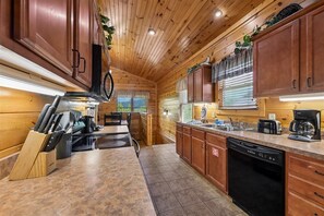 A kitchen with wooden cabinets, a dishwasher, and a countertop with various appliances. - Modern Mountain Getaway w/ Hot Tub & Arcade (Gatlinburg)