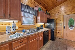 A kitchen with wooden cabinets, a refrigerator, a coffee maker, and a sink. - Modern Mountain Getaway w/ Hot Tub & Arcade (Gatlinburg)