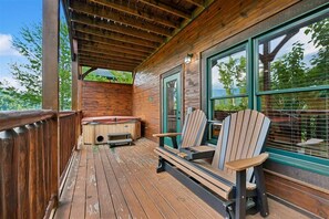 A wooden deck with a hot tub, two Adirondack chairs, and a window with a view of trees. - Modern Mountain Getaway w/ Hot Tub & Arcade (Gatlinburg)