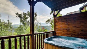 En træterrasse med jacuzzi, trægelænder og udsigt til bjerge og træer.