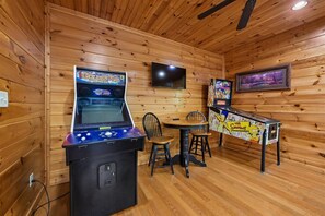 A wooden interior with arcade games, a television, and a table with a Simpsons-themed tablecloth. - Modern Mountain Getaway w/ Hot Tub & Arcade (Gatlinburg)