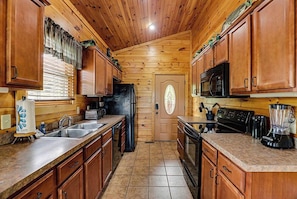 A wooden-paneled kitchen with a refrigerator, stove, microwave, and coffee maker.