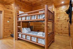 A bunk bed with a wooden frame and patterned bedding in a cabin-style room with wooden walls and floors. - Modern Mountain Getaway w/ Hot Tub & Arcade (Gatlinburg)