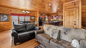 A log cabin interior with a dining area, kitchen, and two sofas with deer prints. - Mountain Cabin w/ Theater, Games & Views (Gatlinburg)