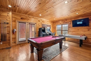 A wooden interior with a pool table, a billiards table, and a television mounted on the wall.