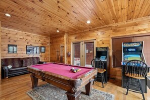 A wooden interior with a pool table, a sofa, and a gaming machine.