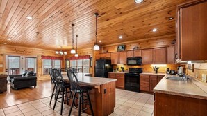A spacious kitchen with wooden cabinets, a central island with bar stools, and a dining area with a couch and chairs. - Mountain Cabin w/ Theater, Games & Views (Gatlinburg)