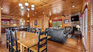 A wooden cabin interior with a dining area, a living room with a sofa, a fireplace, and a television mounted on the wall. - Mountain Cabin w/ Theater, Games & Views (Gatlinburg)