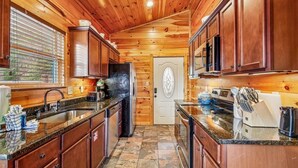 Un interior de madera con una cocina que presenta encimeras de granito, armarios de madera y un suelo de baldosas de piedra.