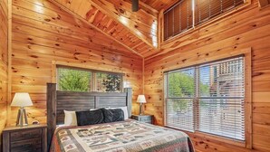 Un dormitorio acogedor de cabaña de madera, con una cama, dos mesitas de noche y un ventanal con persianas.