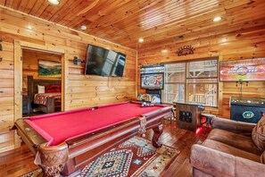 A wooden cabin with a pool table, a sofa, and a television mounted on the wall.