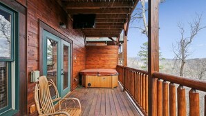 Une cabane en bois dotée d’une terrasse en bois, d’un bain à remous et d’une chaise.