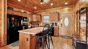 Une cuisine de style rustique, avec des éléments en bois, comprenant un îlot central, des armoires en bois, un réfrigérateur et un four à micro-ondes.