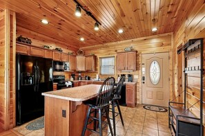 Una cocina estilo cabaña de madera con una isla central, armarios de madera, un refrigerador y un microondas.