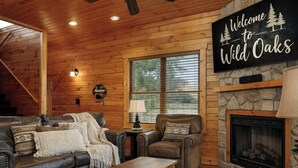 Un intérieur de chalet chaleureux avec un canapé en cuir, une table basse en bois, une cheminée et une pancarte indiquant : « Bienvenue à Wild Oaks ».