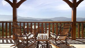 A wooden deck with two rocking chairs and a table, overlooking a mountainous landscape.